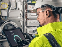man-electrical-technician-working-switchboard-with-fuses-uses-tablet (1)