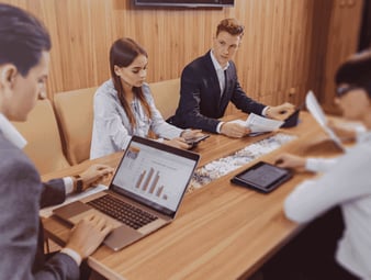office-workers-hold-meeting-one-desk-laptops-tablets-papers-large-tv-set-wooden-wall